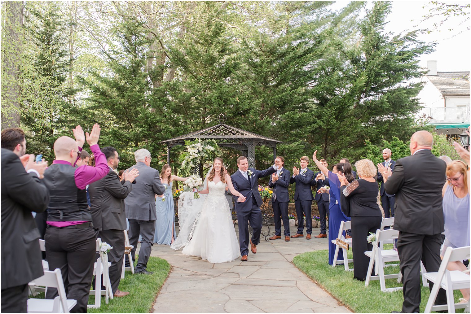 bride and groom hold hands walking up the aisle after garden wedding ceremony 