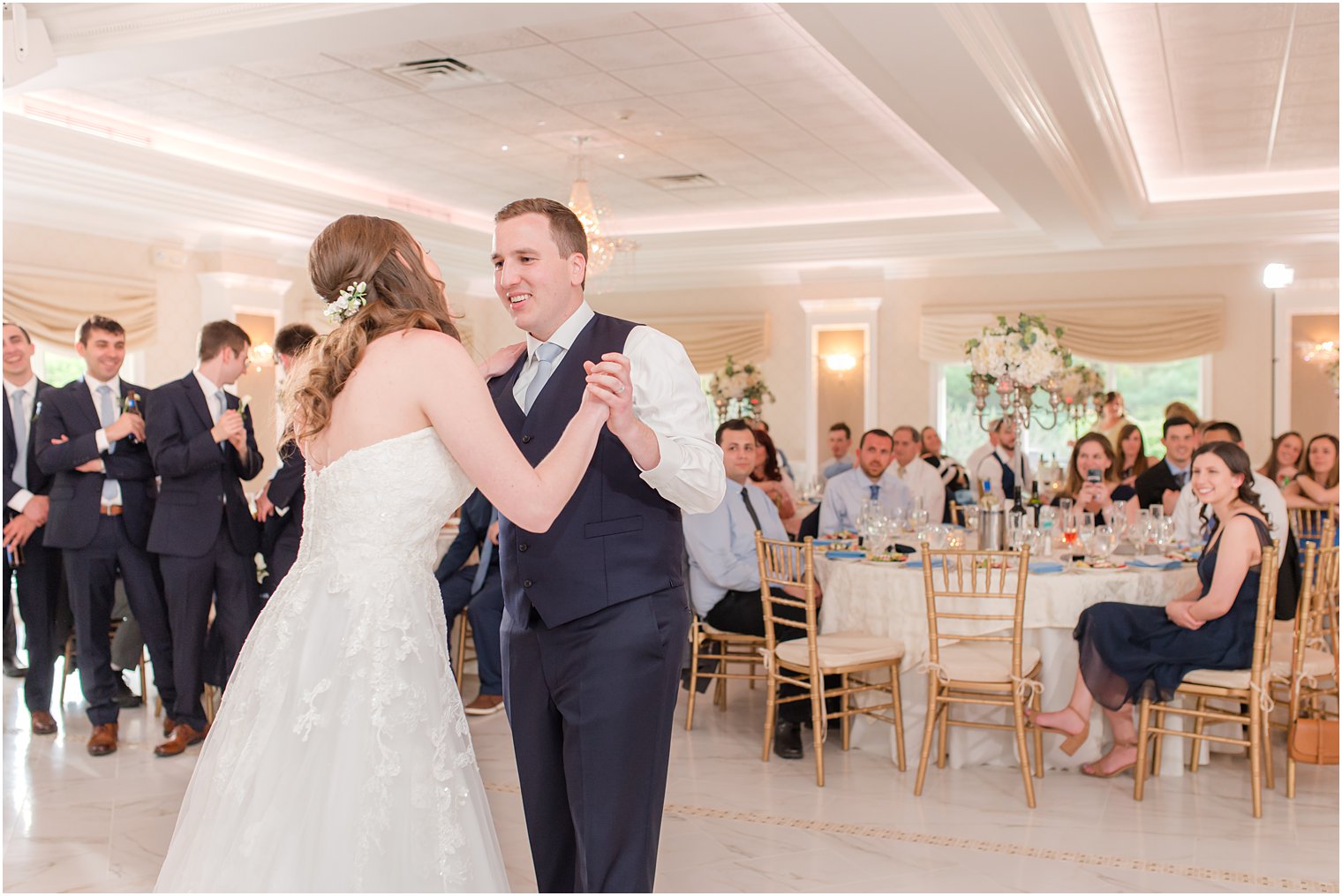 groom in navy vest dances with bride in ballroom