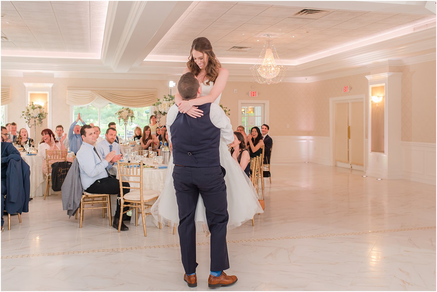 groom in navy vest lifts with bride in ballroom