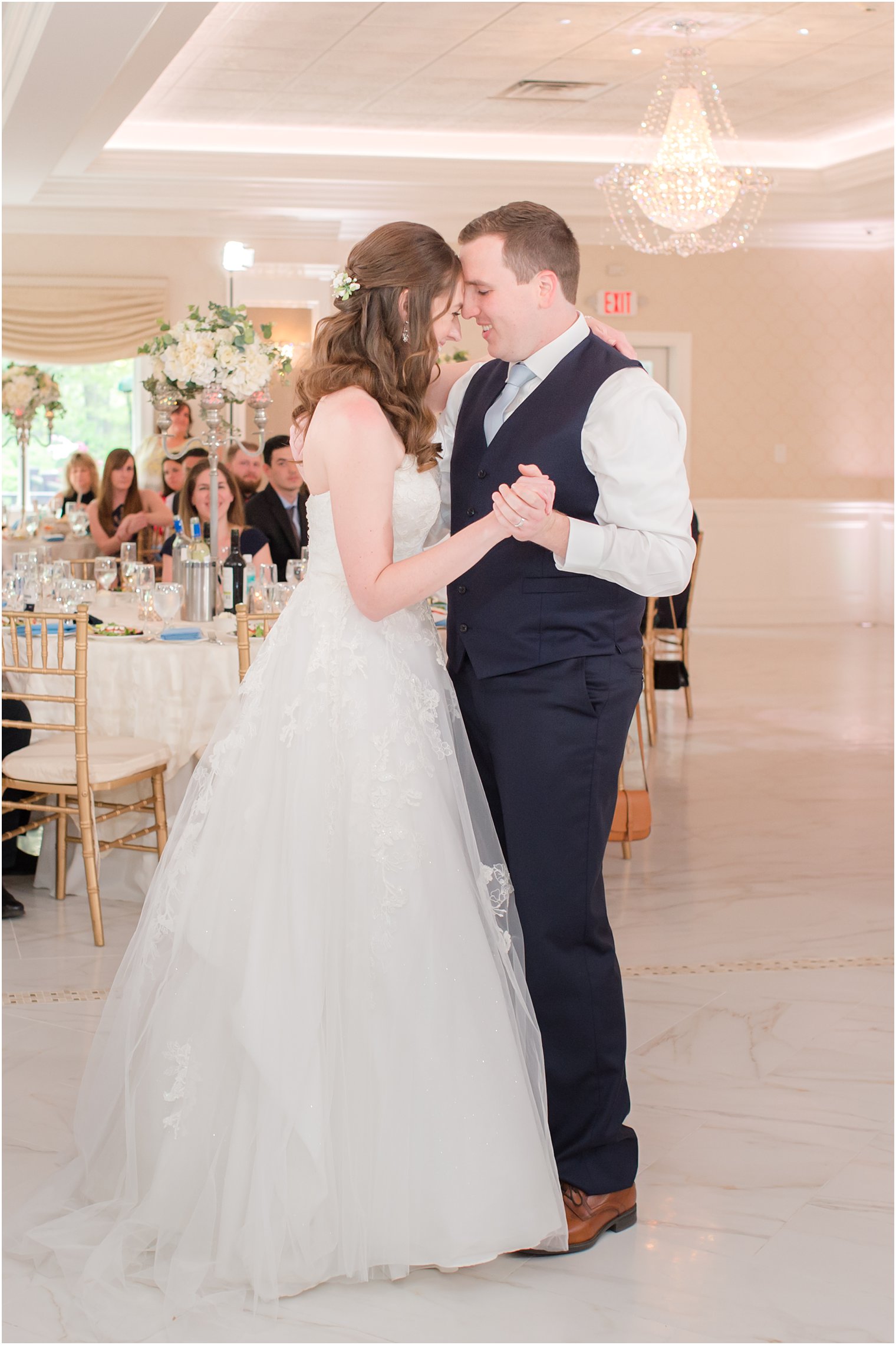 groom in navy vest dances with bride in ballroom