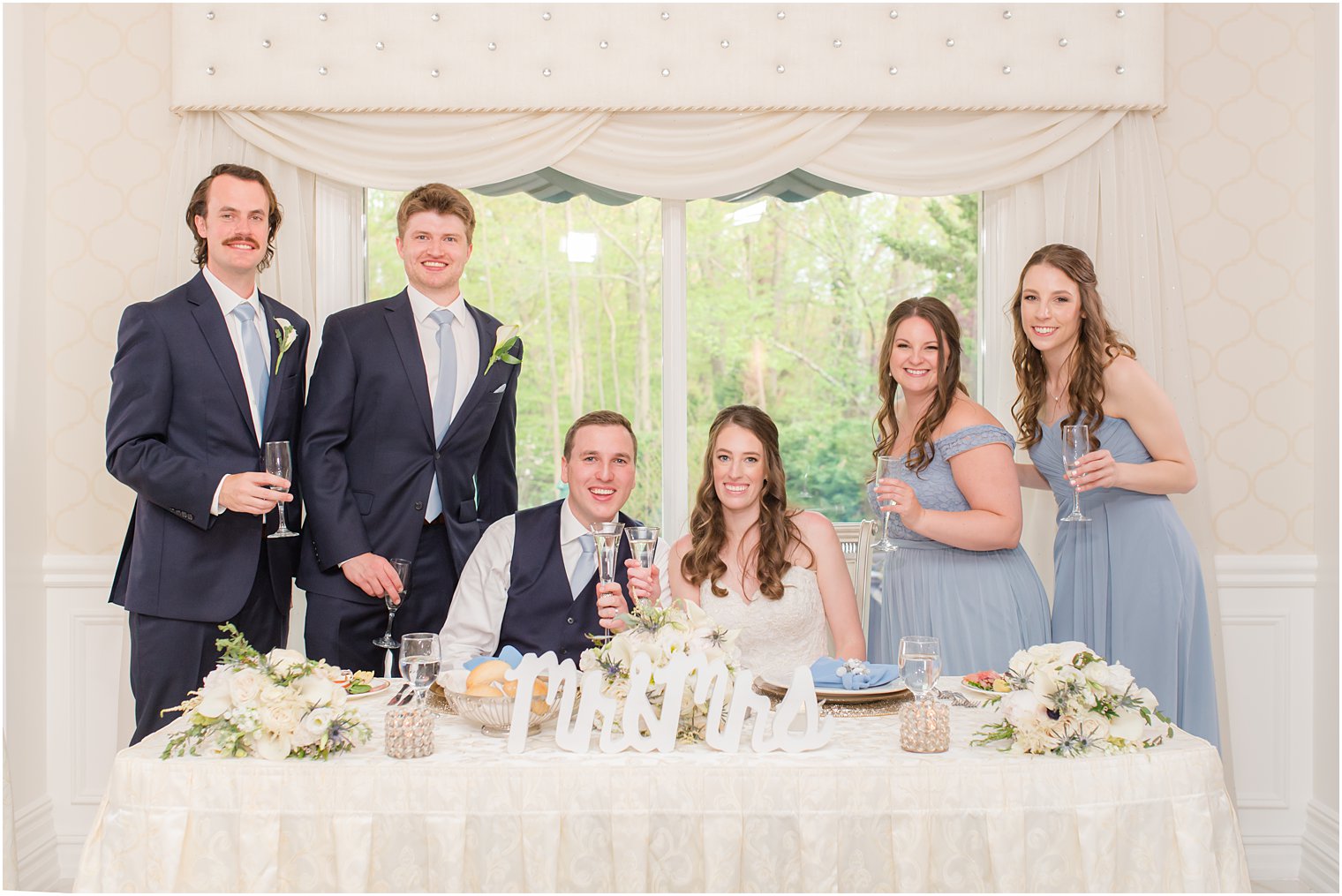 bride and groom sit at sweetheart table with bridesmaids and groomsmen 