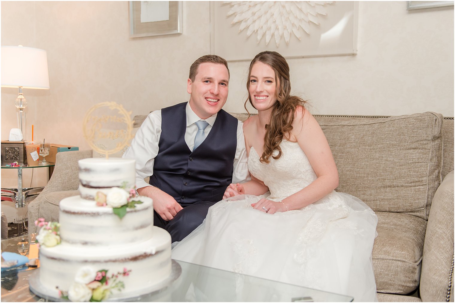 bride and groom sit on couch behind wedding cake at The English Manor