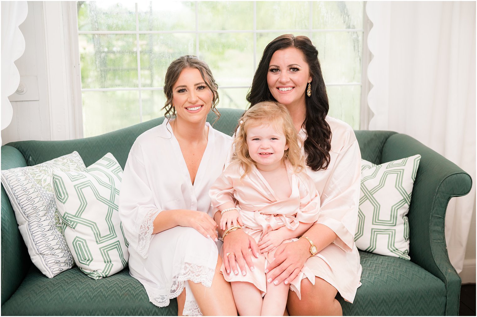bride sits on green couch with bridesmaid and flower girl