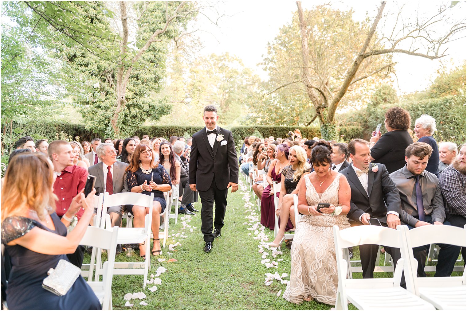 groom walks down aisle for ceremony in garden at The Inn at Fernbrook Farms