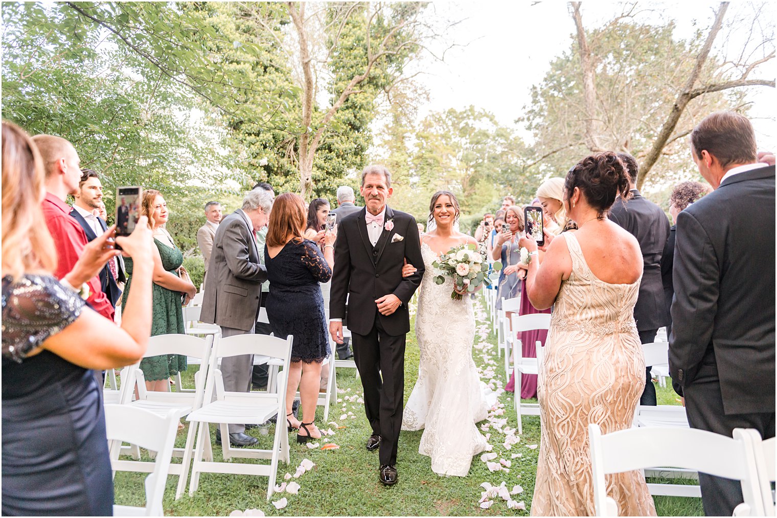 father in black tux walks bride down aisle for wedding ceremony in garden at The Inn at Fernbrook Farms