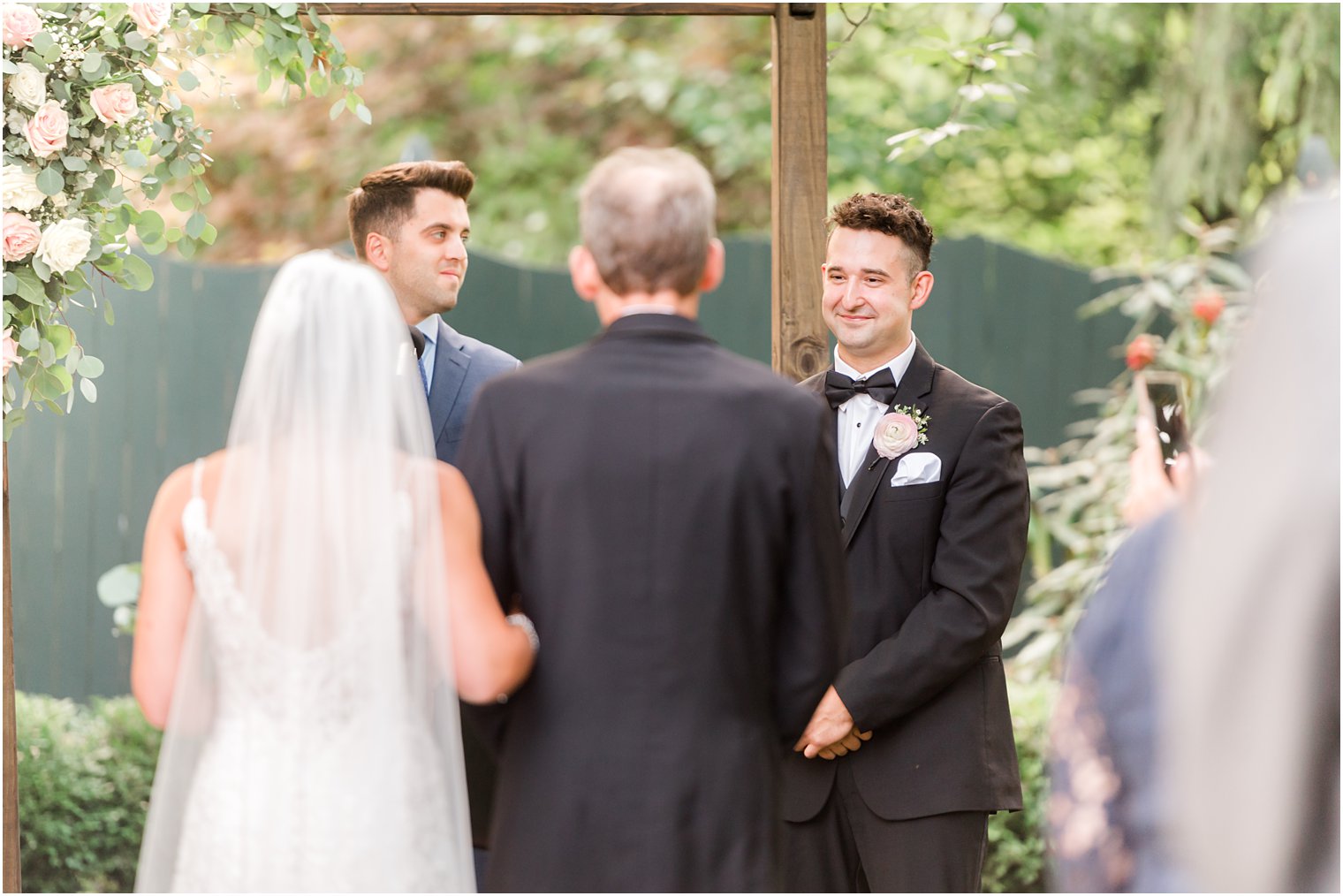 groom smiles at bride and dad before wedding ceremony in garden at The Inn at Fernbrook Farms