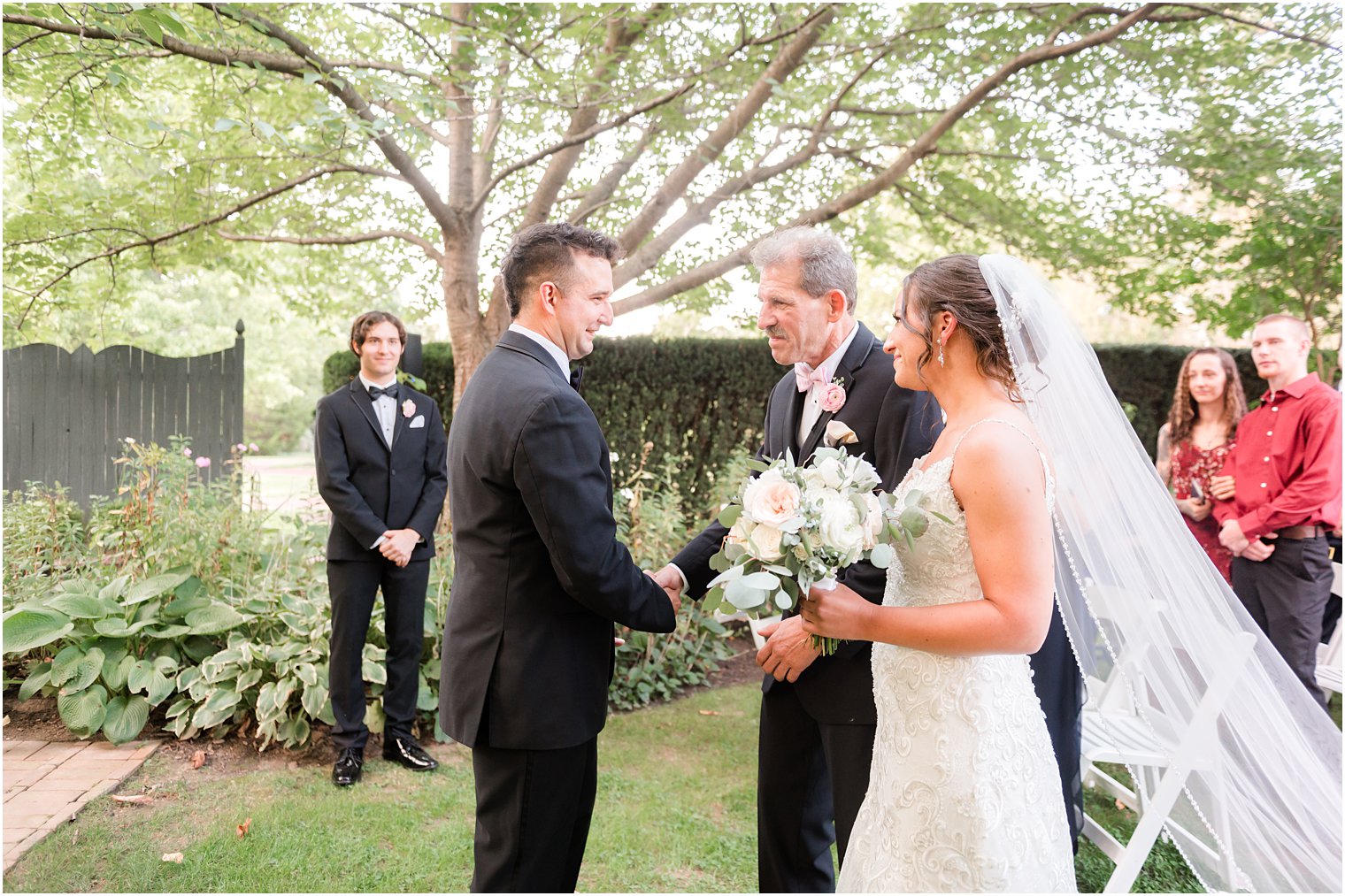 groom shakes hand with father-in-law during wedding ceremony in garden at The Inn at Fernbrook Farms
