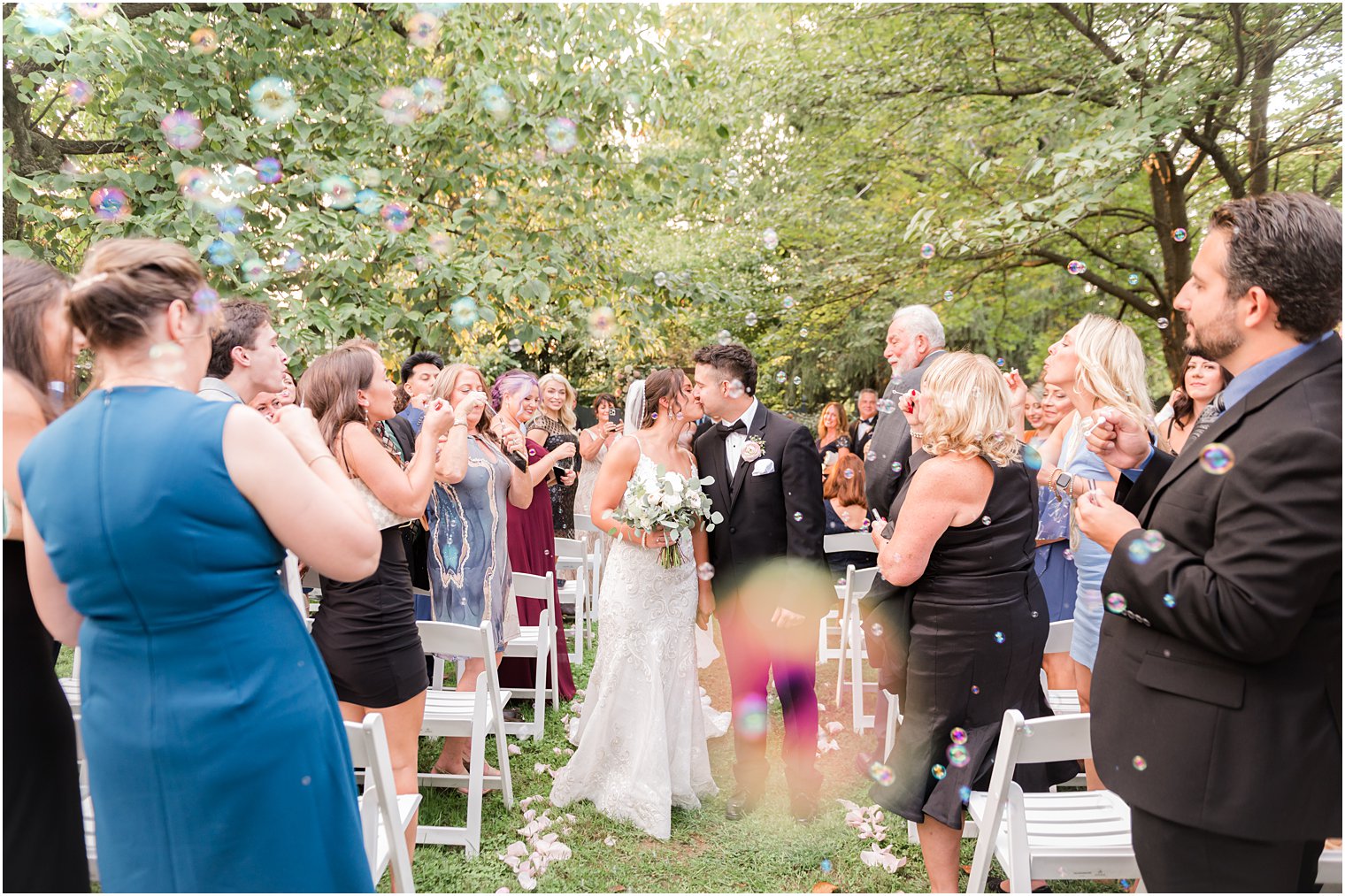 groom kisses bride's hair in aisle during bubble exit from wedding ceremony in garden at The Inn at Fernbrook Farms