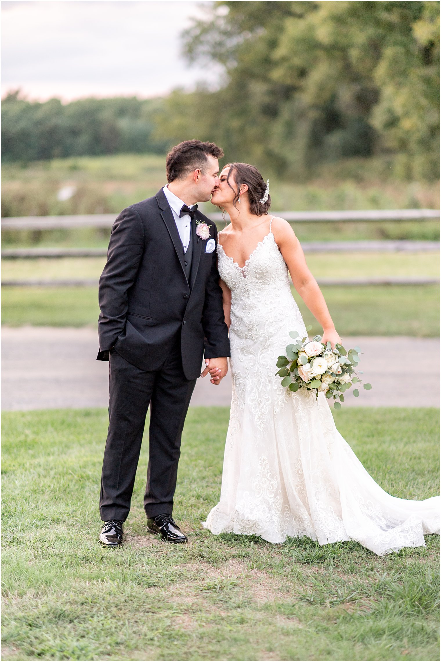 bride and groom kiss along wooden fence at The Inn at Fernbrook Farms