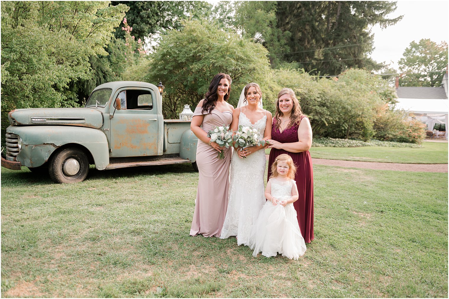 bridesmaids stand with bride by vintage green truck outside The Inn at Fernbrook Farms