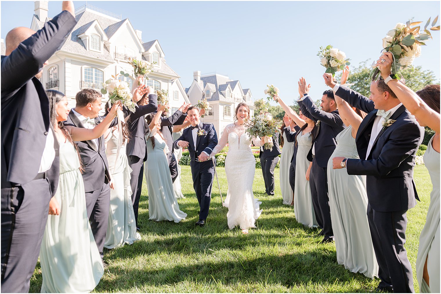 newlyweds smile walking between wedding party cheering on lawn