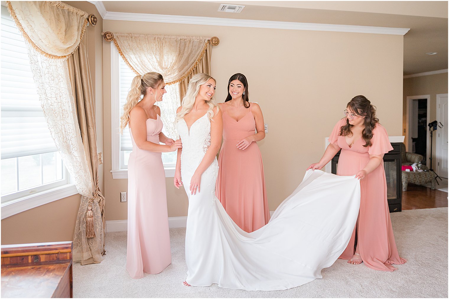 bridesmaids in pink gowns helps bride with wedding dress in NJ home 