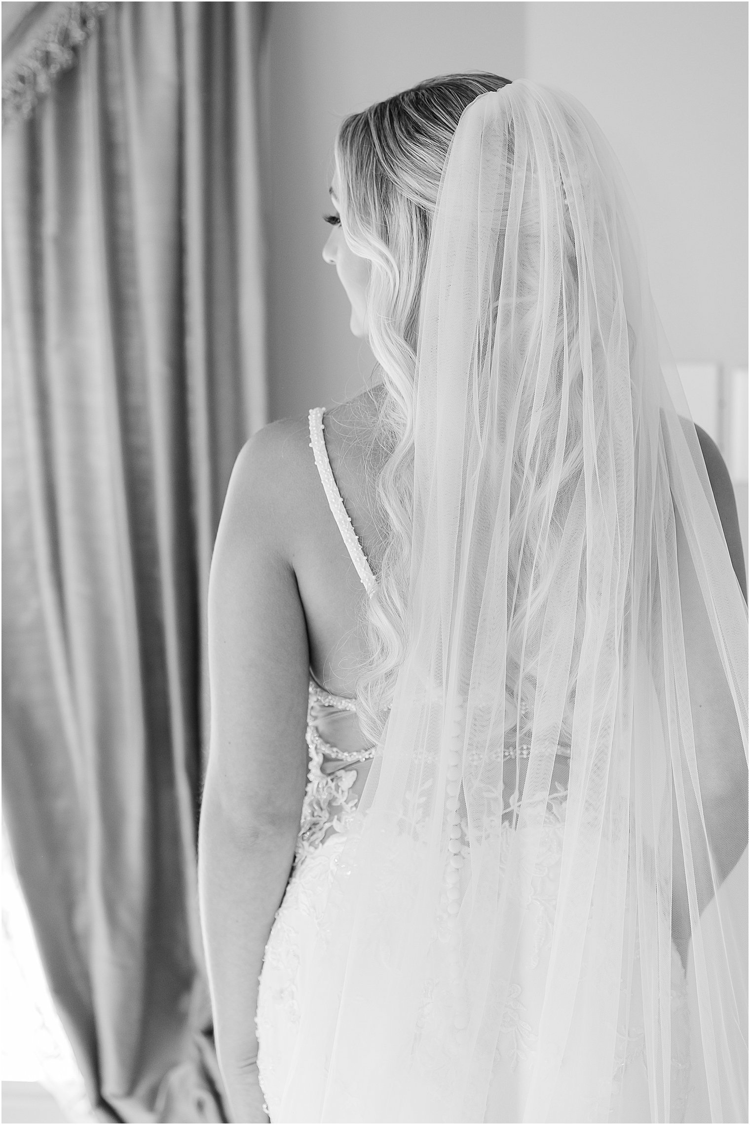 black and white portrait of bride looking out window with veil behind her