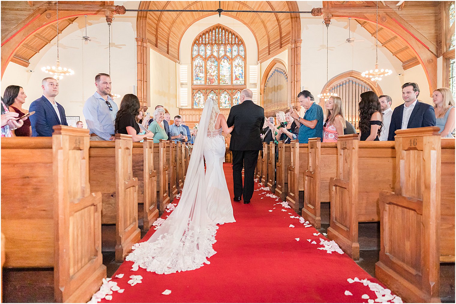 bride walks down aisle on red carpet with father during traditional church wedding in New Jersey
