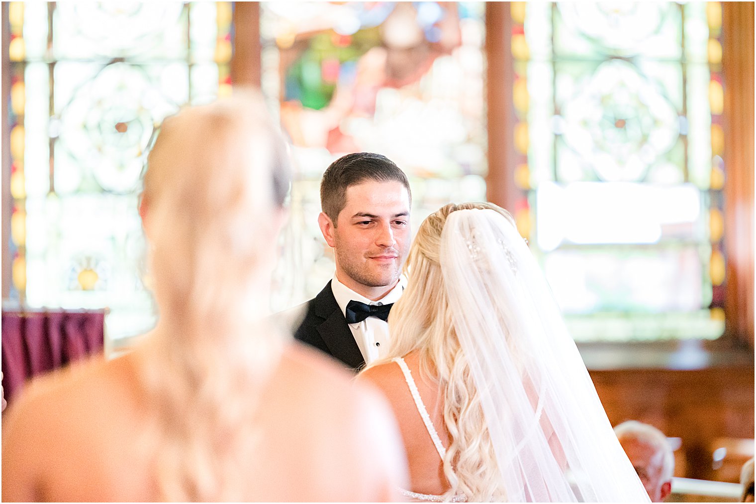 groom smiles at bride standing holding hands during traditional church wedding in New Jersey