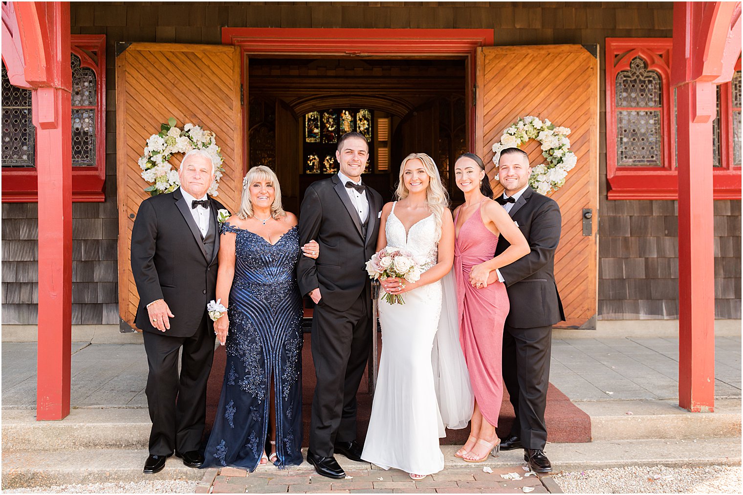 bride and groom pose with family outside wooden church in New Jersey