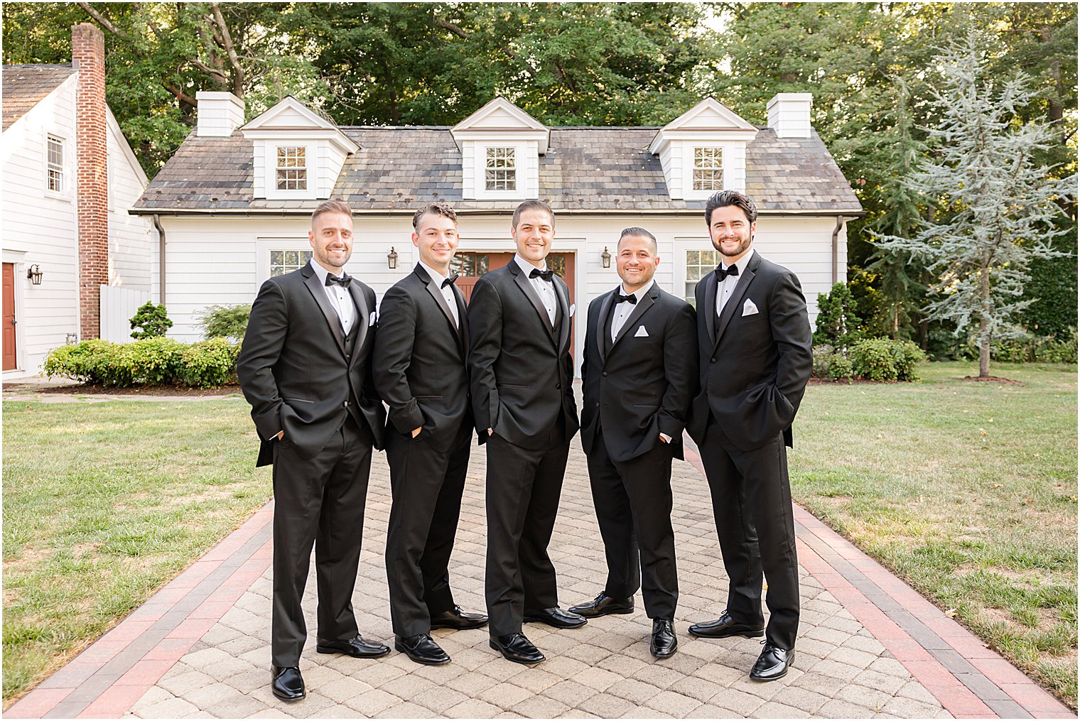 groom stands with groomsmen standing by house at The English Manor