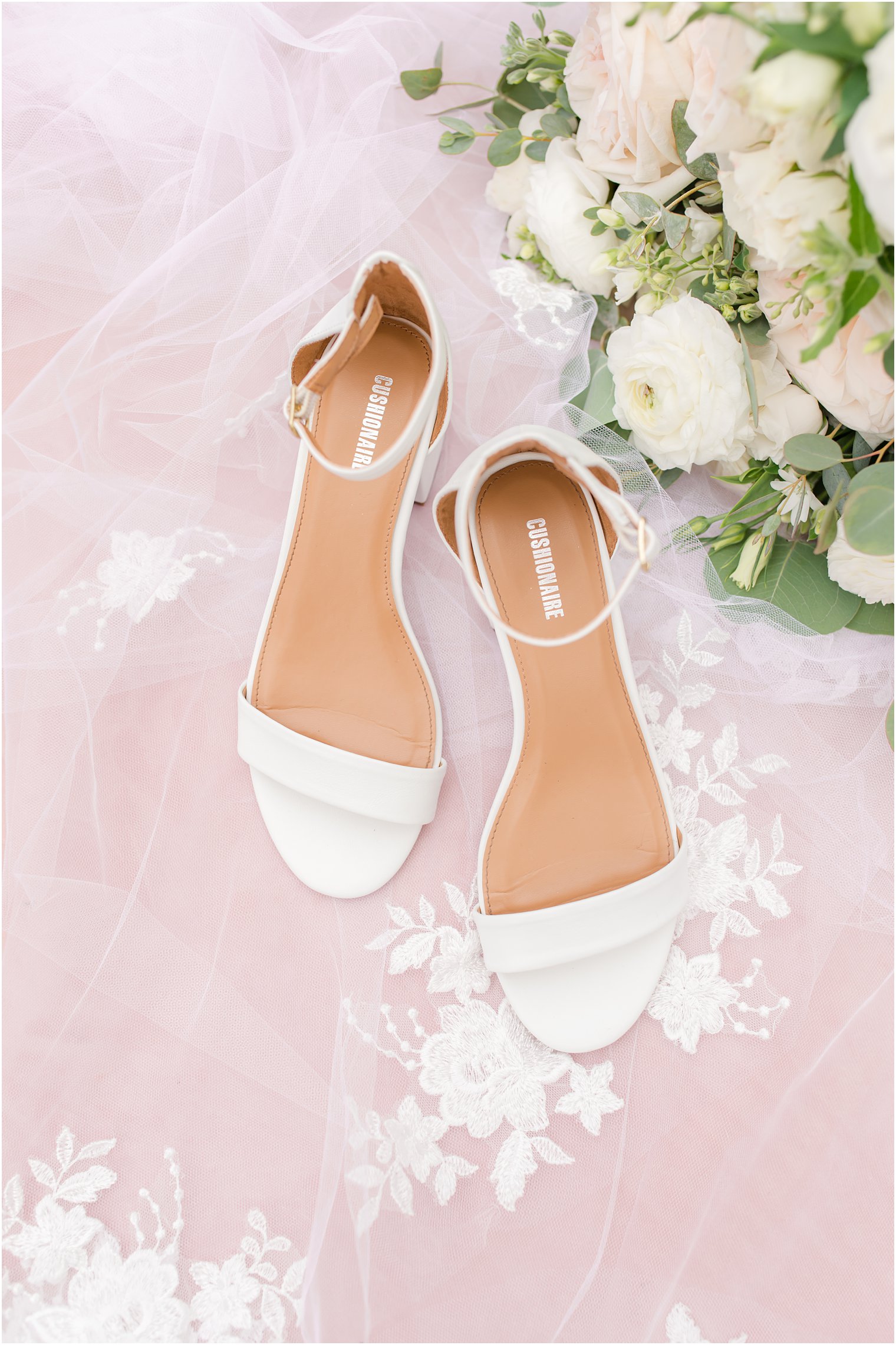 bride's white shoes rest on lace veil 