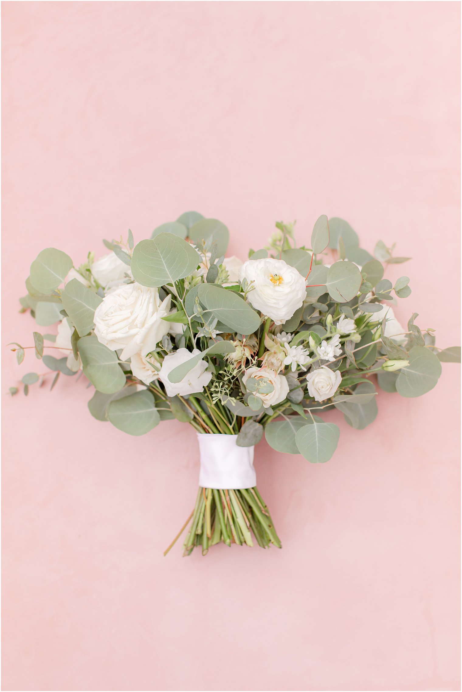 bridal bouquet with white flowers and greenery on pink background 