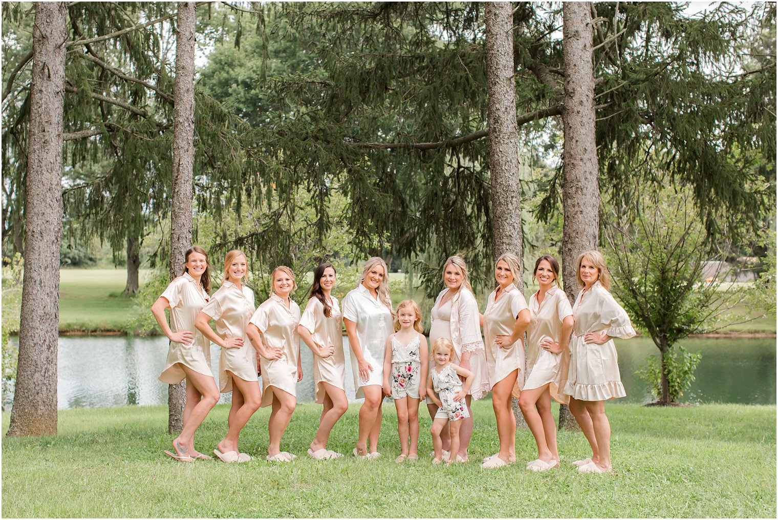 bride poses with bridesmaids in pink robes on lawn at Windows on the Water at Frogbridge