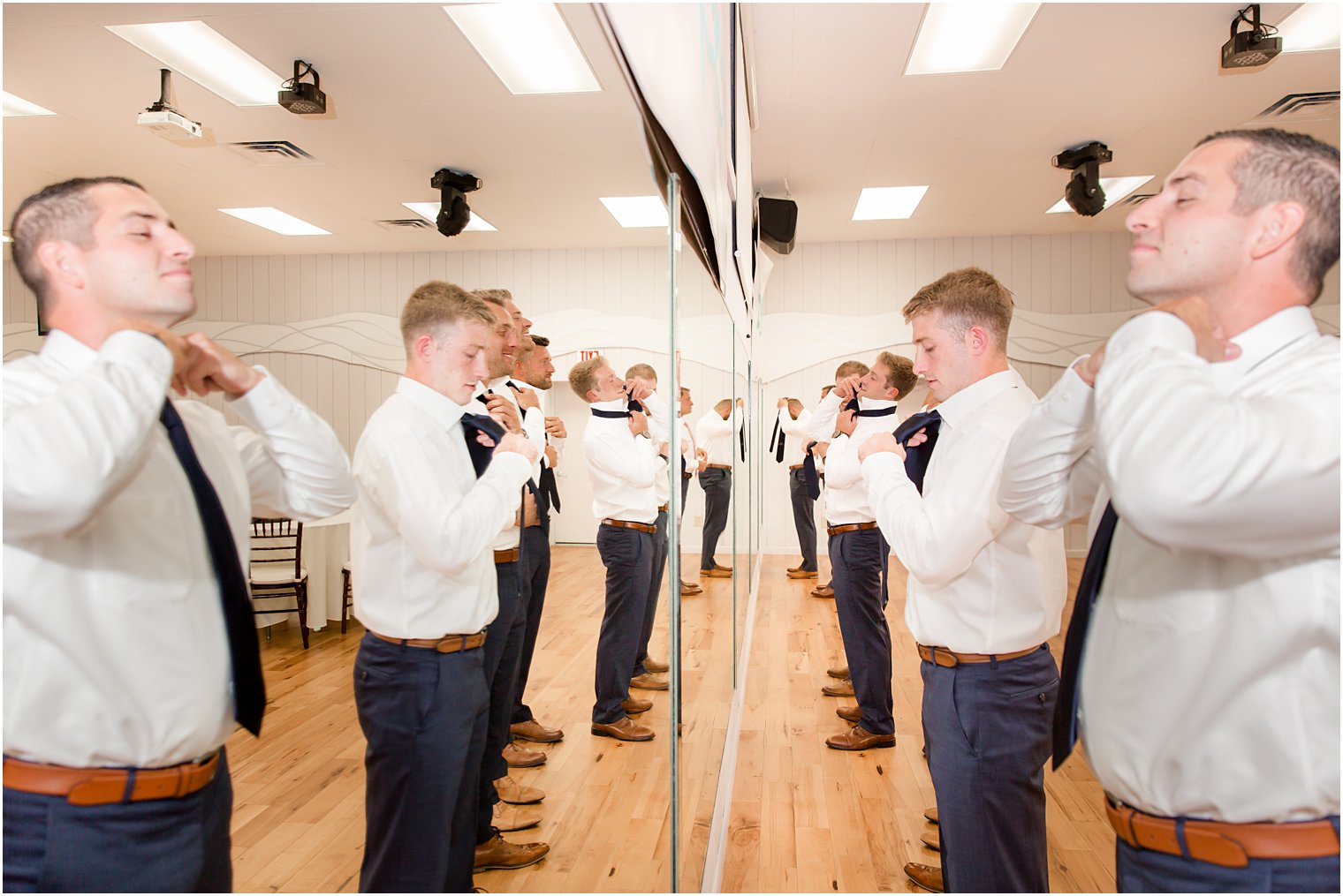 groom and groomsmen prepare for wedding in front of mirrored wall 