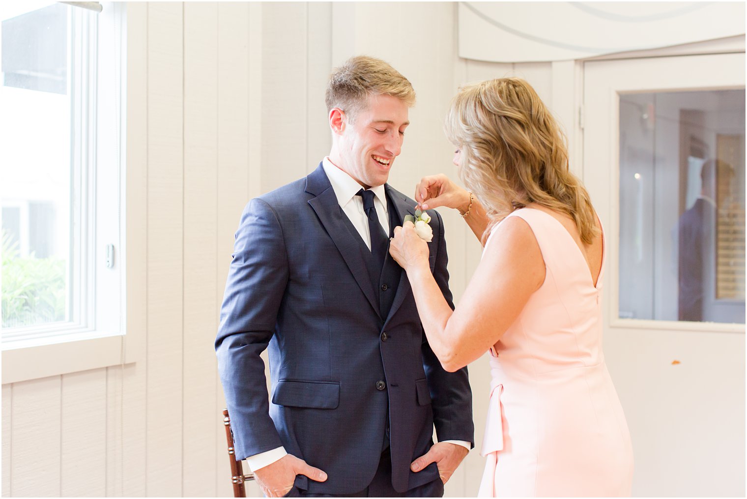 mother in pink dress helps groom with boutonniere 