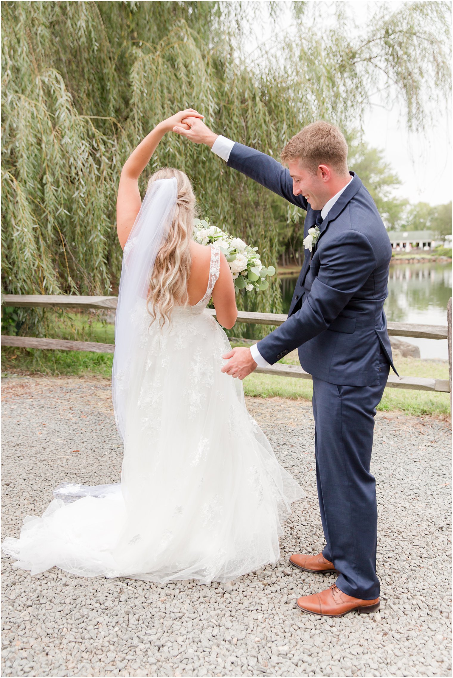groom twirls bride by wooden fence at Windows on the Water at Frogbridge
