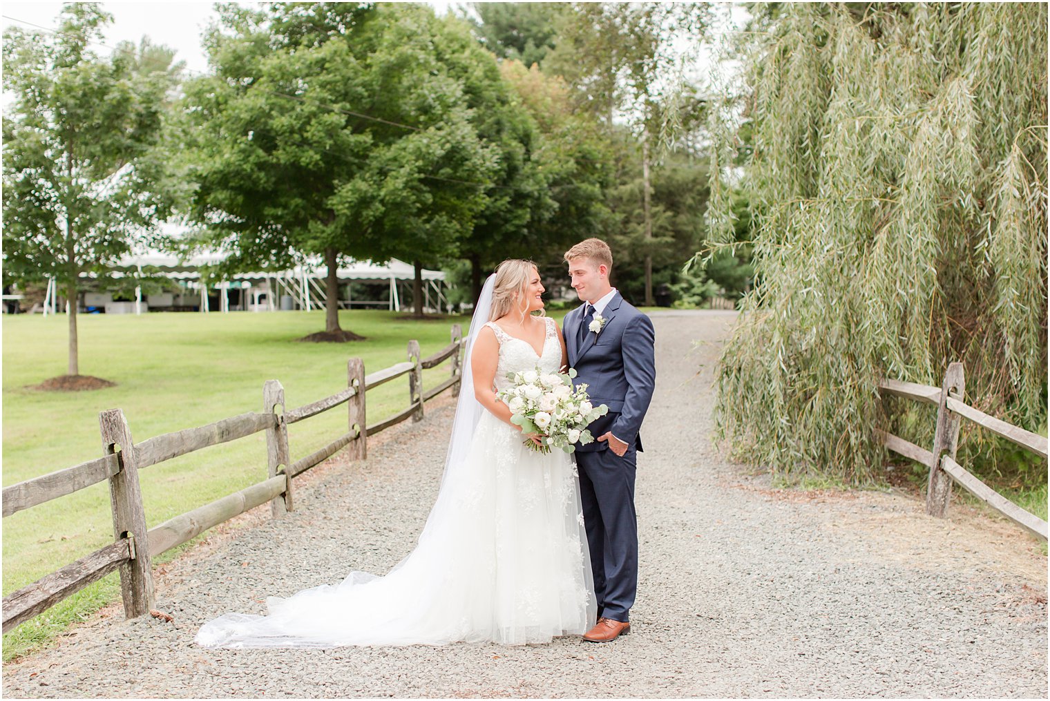 bride and groom stand together in driveway by willow tree at Windows on the Water at Frogbridge
