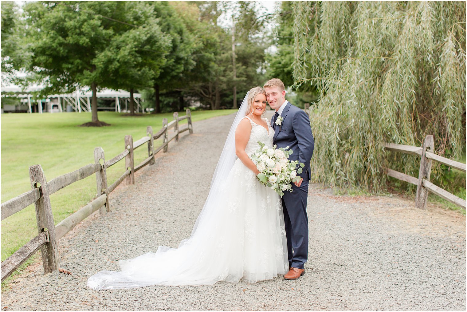 newlyweds stand with heads touching near willow tree at Windows on the Water at Frogbridge