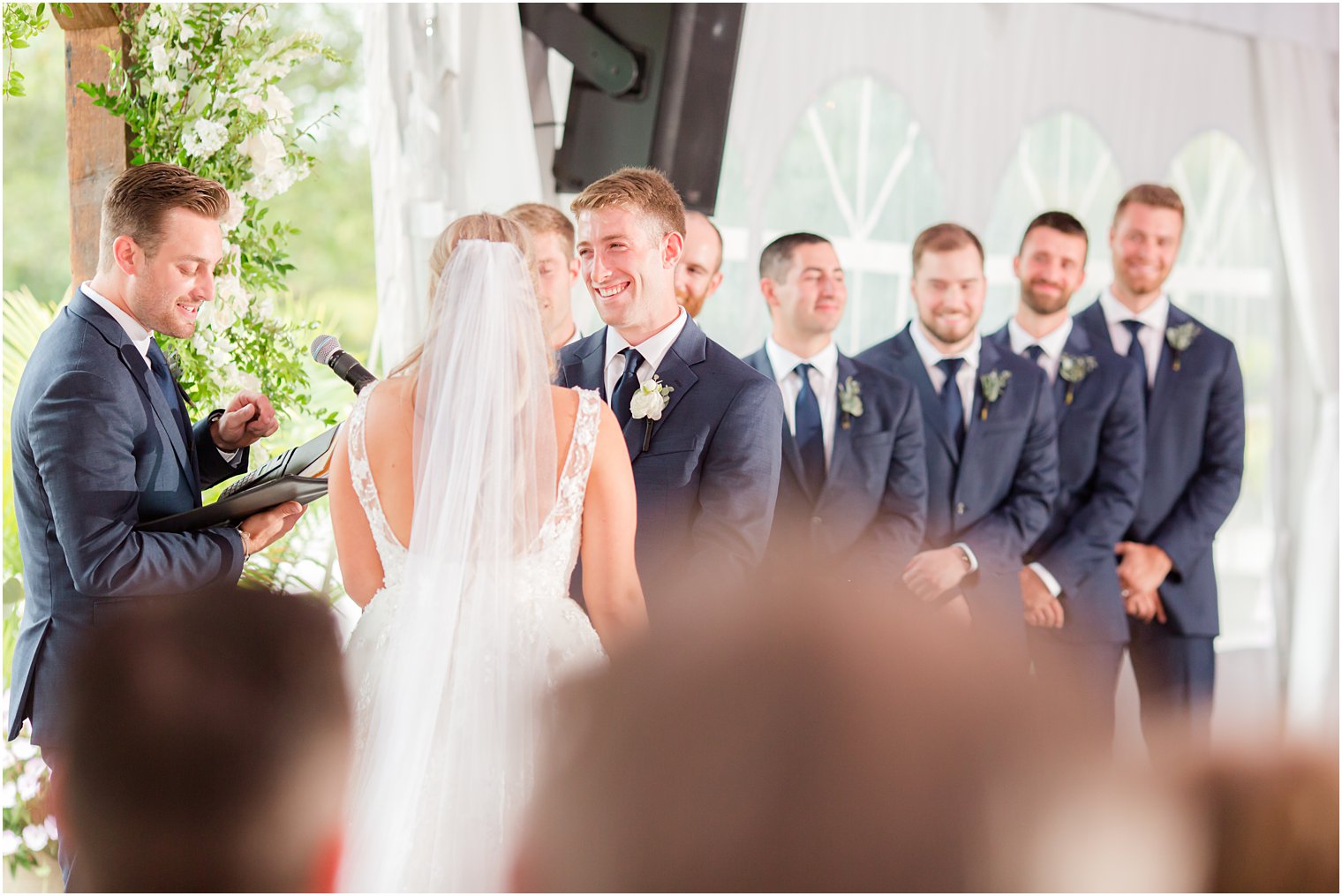 groom smiles at bride during tented wedding ceremony at Windows on the Water at Frogbridge