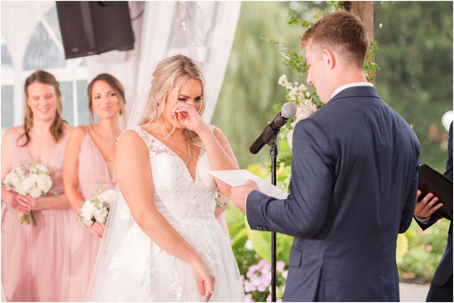 bride wipes away tear during tented wedding ceremony at Windows on the Water at Frogbridge