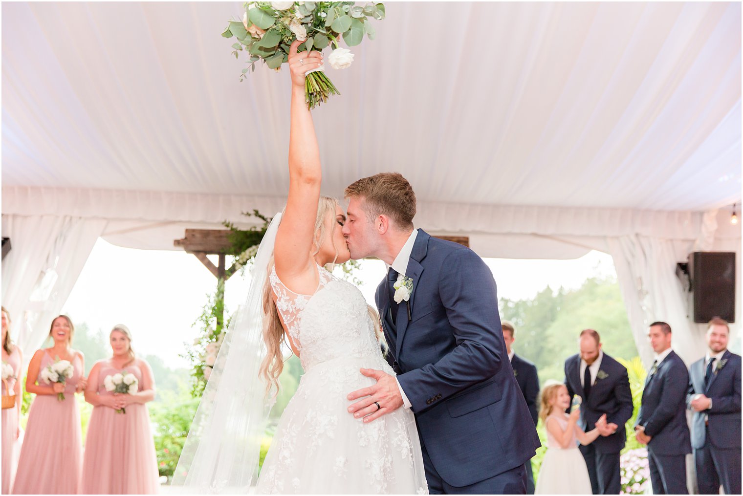 bride and groom kiss while bride pumps bouquet in the air