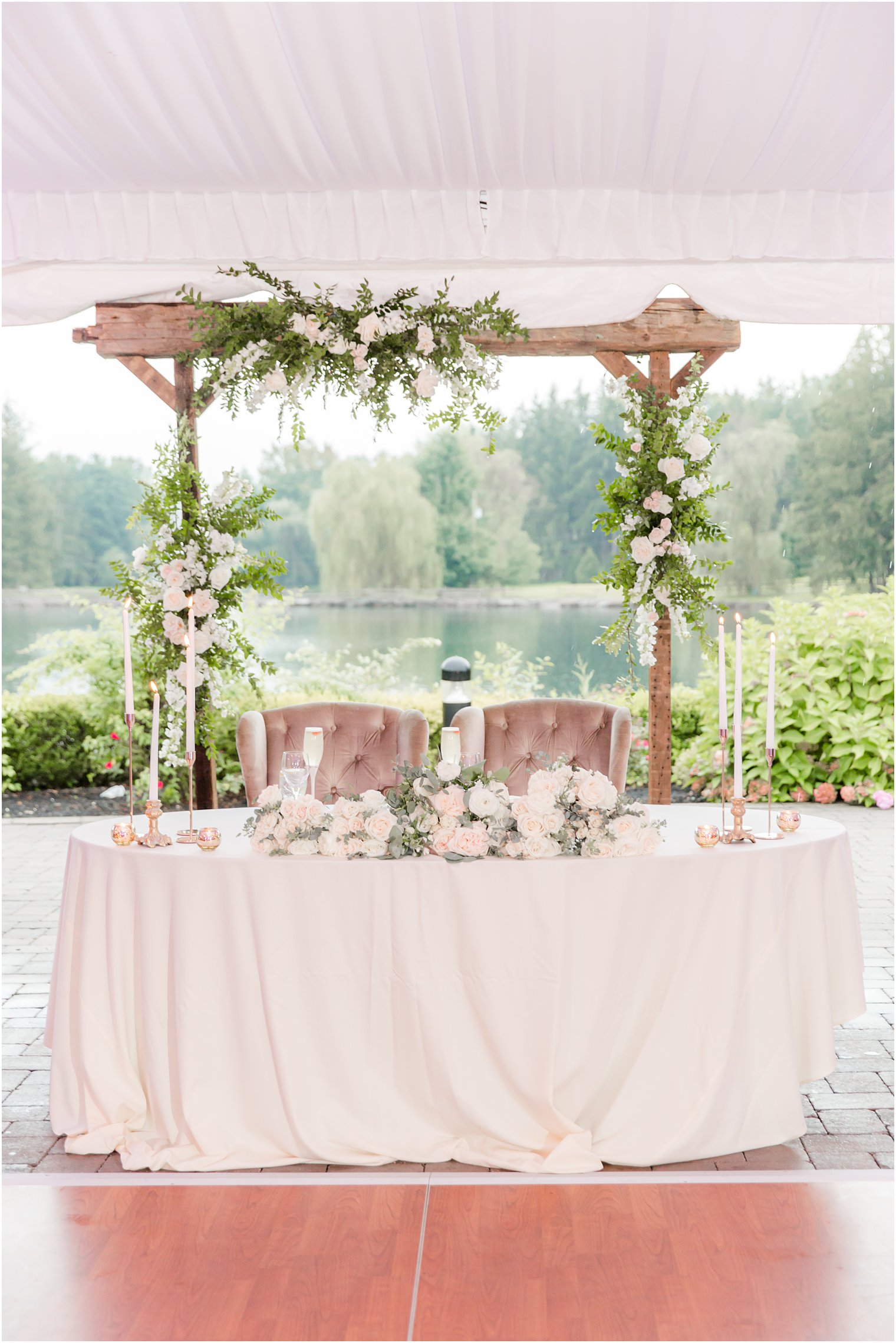 sweetheart table in front of wooden arbor under tent at Windows on the Water at Frogbridge