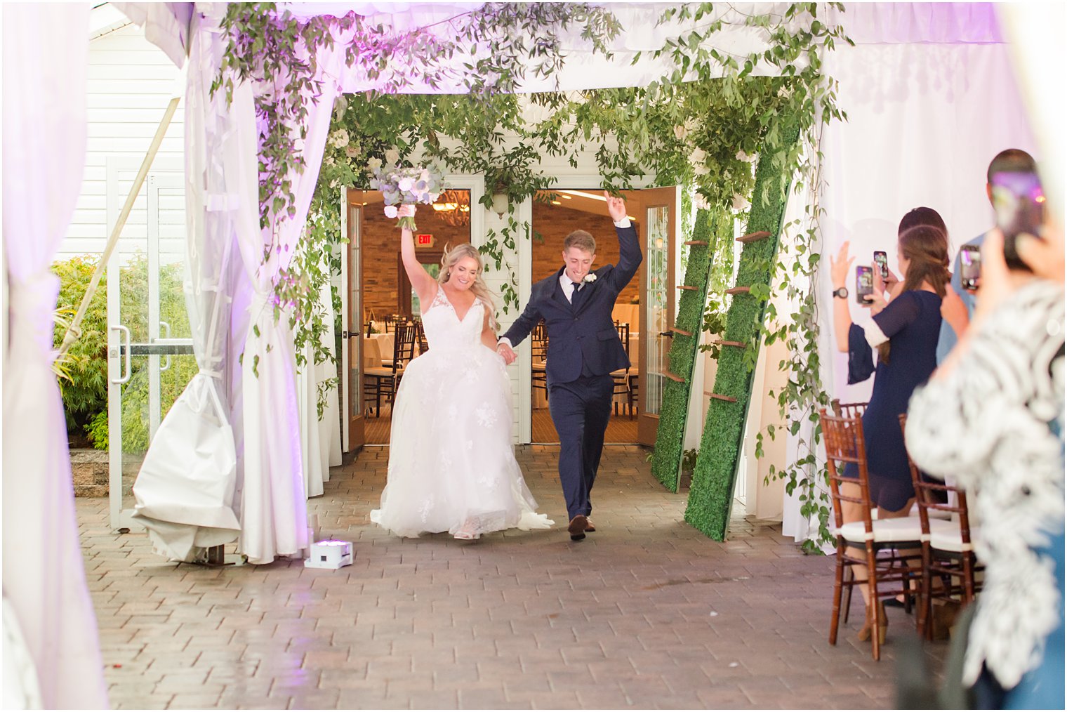 bride and groom wave at guests entering wedding reception 