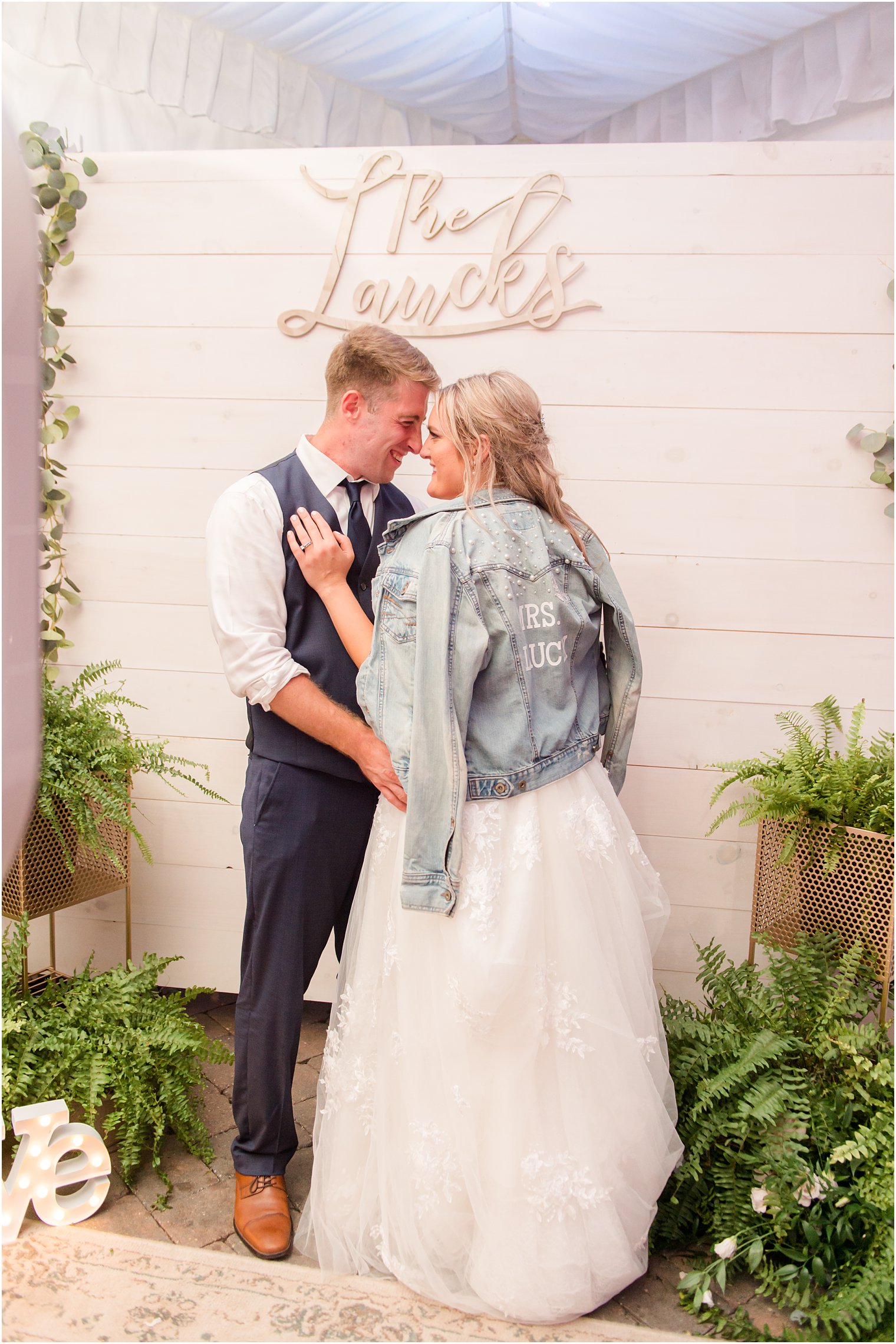 bride and groom hug by white wall and bride wears custom jean jacket