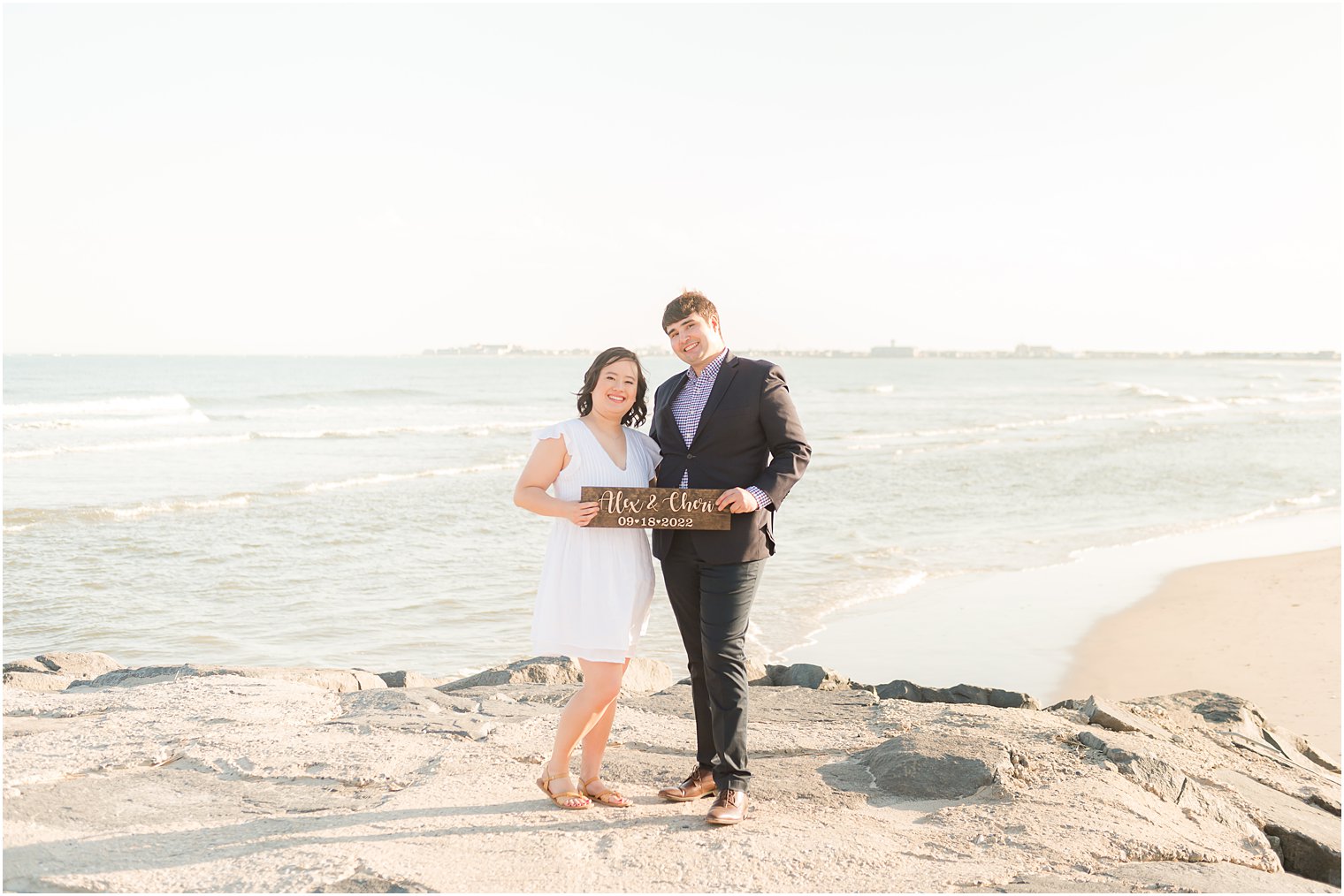 engaged couple holds save-the-date sign standing on rocks 