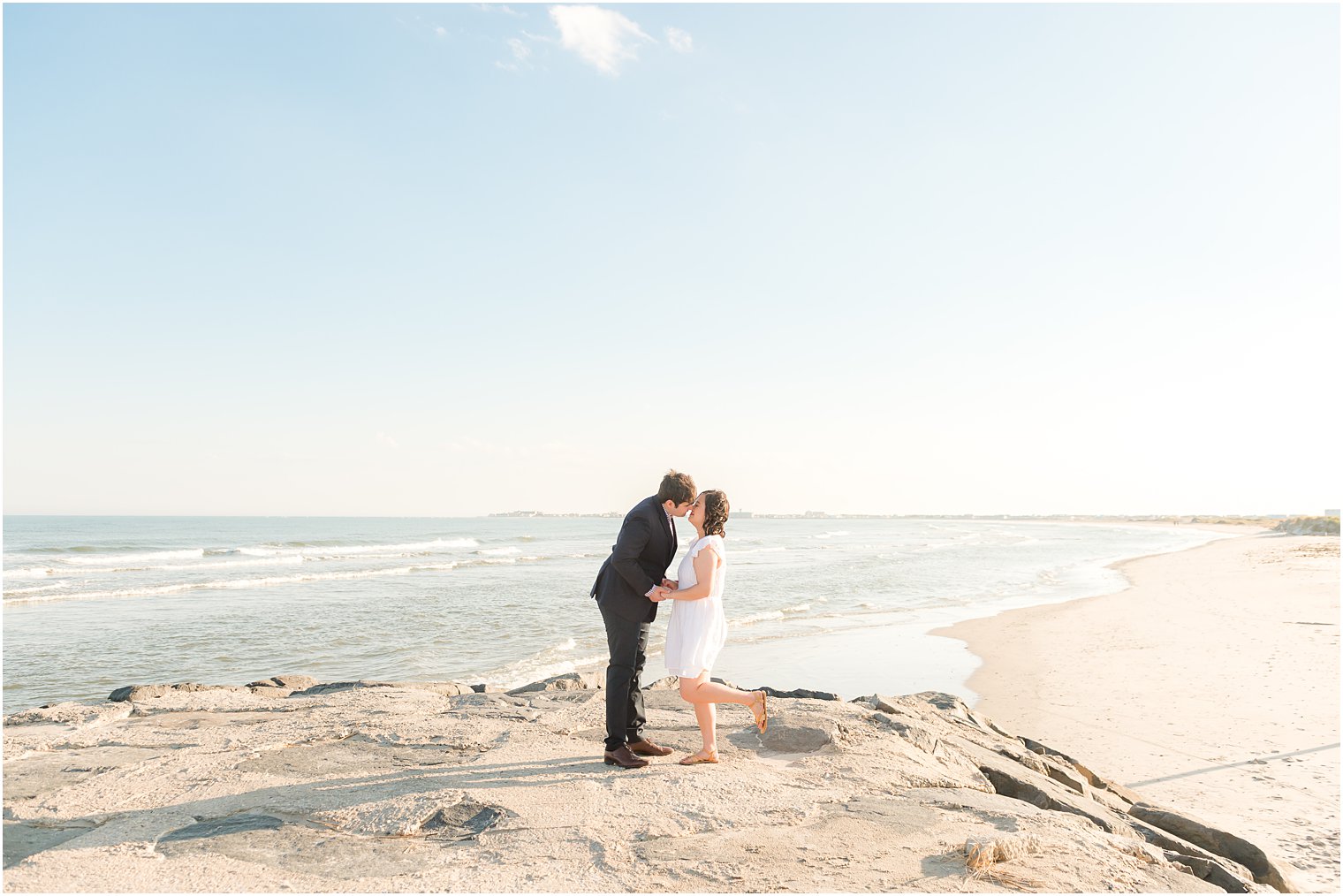 bride and groom kiss on rocks during beach engagement session in Avalon NJ