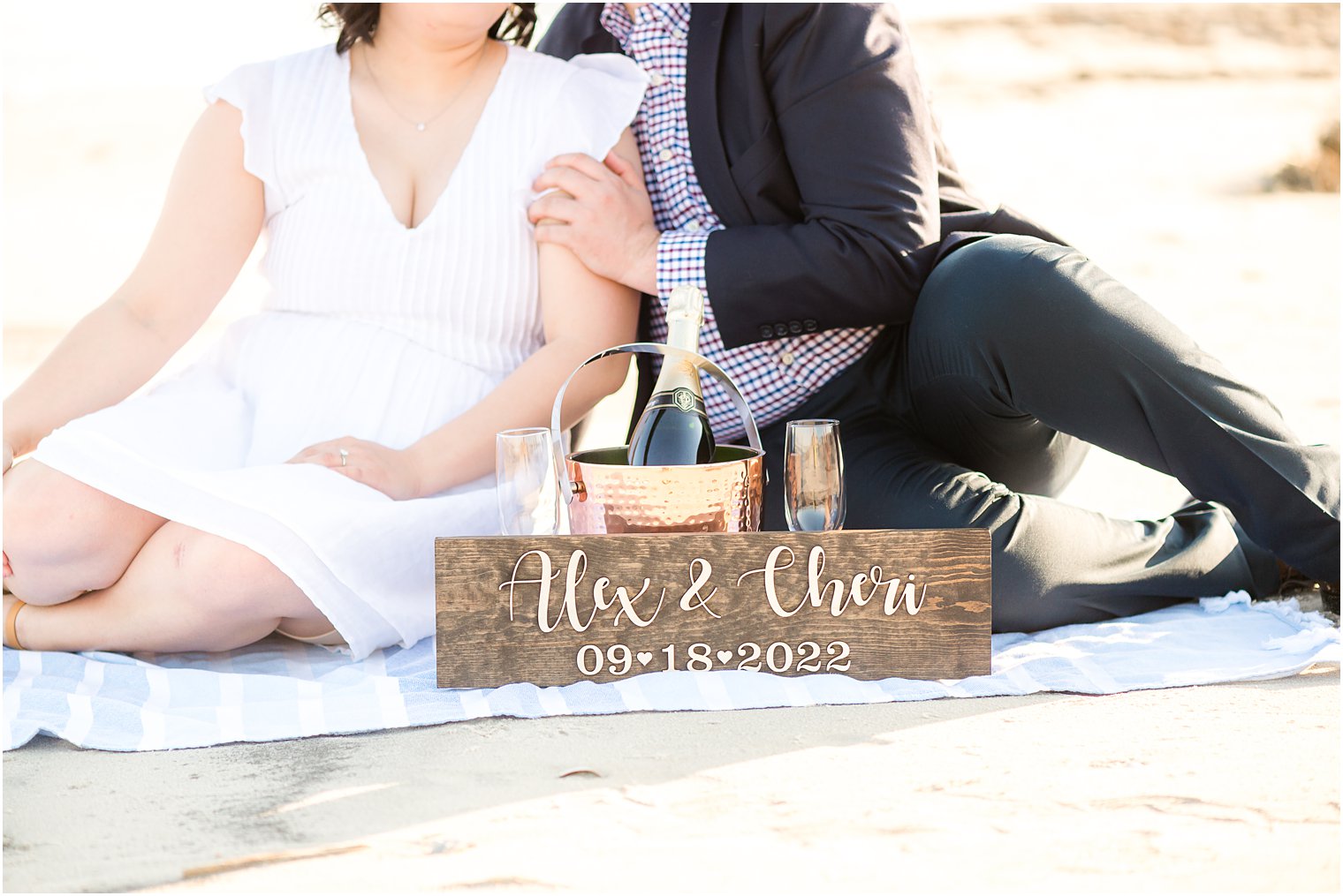 engaged couple sits by save-the-date sign enjoying champagne 