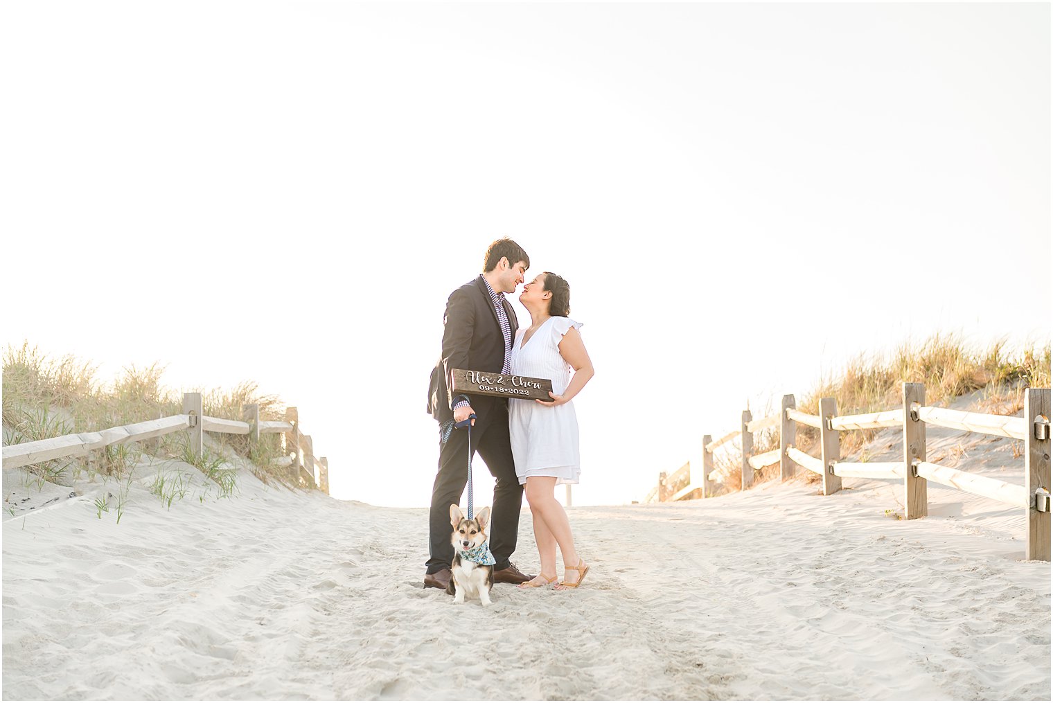 engaged couple stands on sandy path on Avalon NJ beach holding save-the-date sign 
