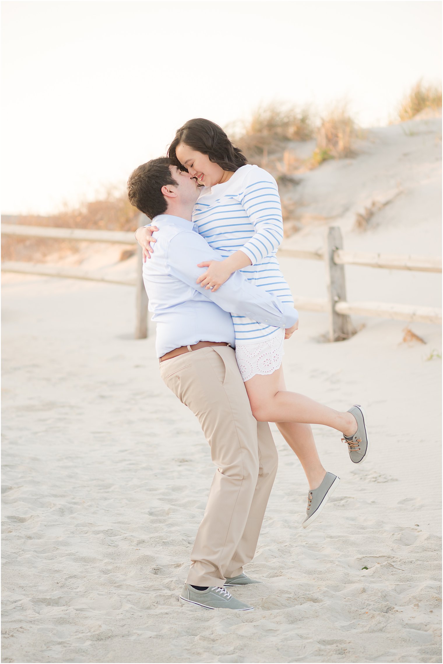 groom lifts bride up during beach engagement session in Avalon NJ