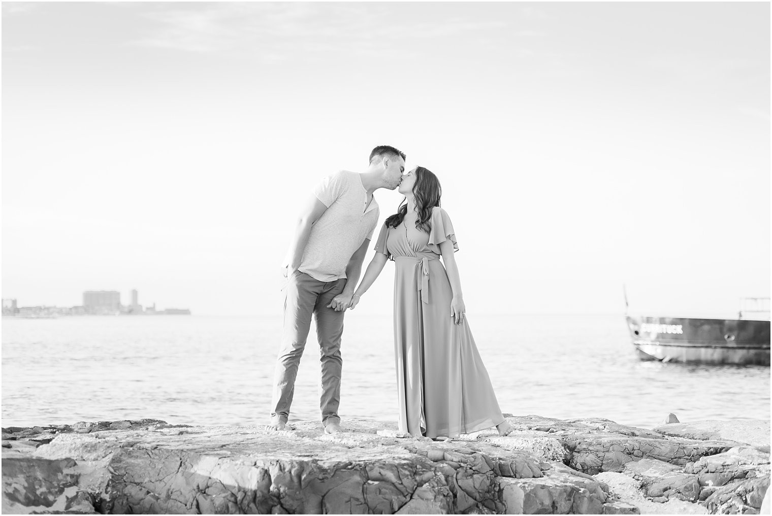 bride and groom lean to kiss each other standing on rocks at the Jersey Shore