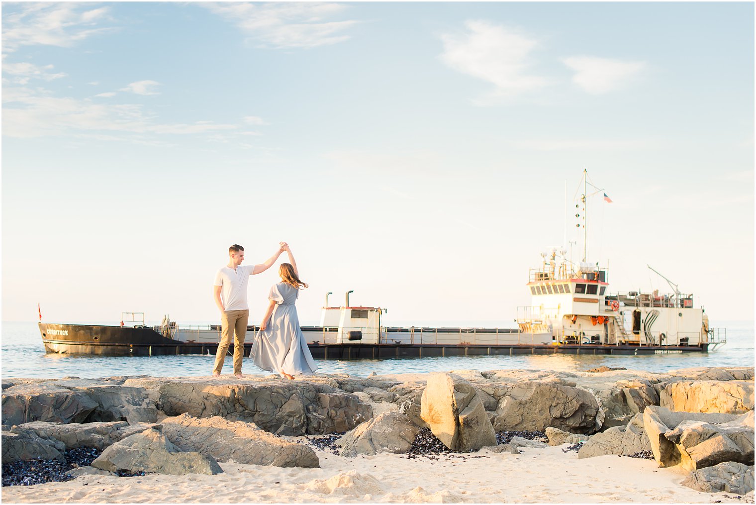 man twirls woman on rocks during Jersey Shore engagement portraits 