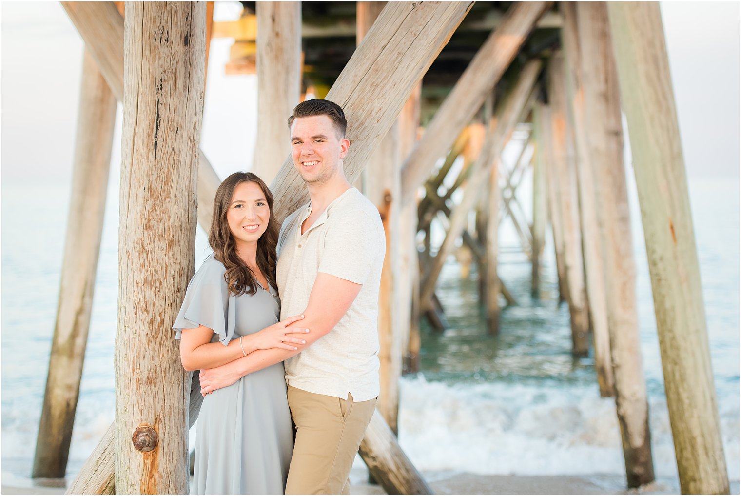 engaged couple hugs against wooden pillars on the Jersey Shore