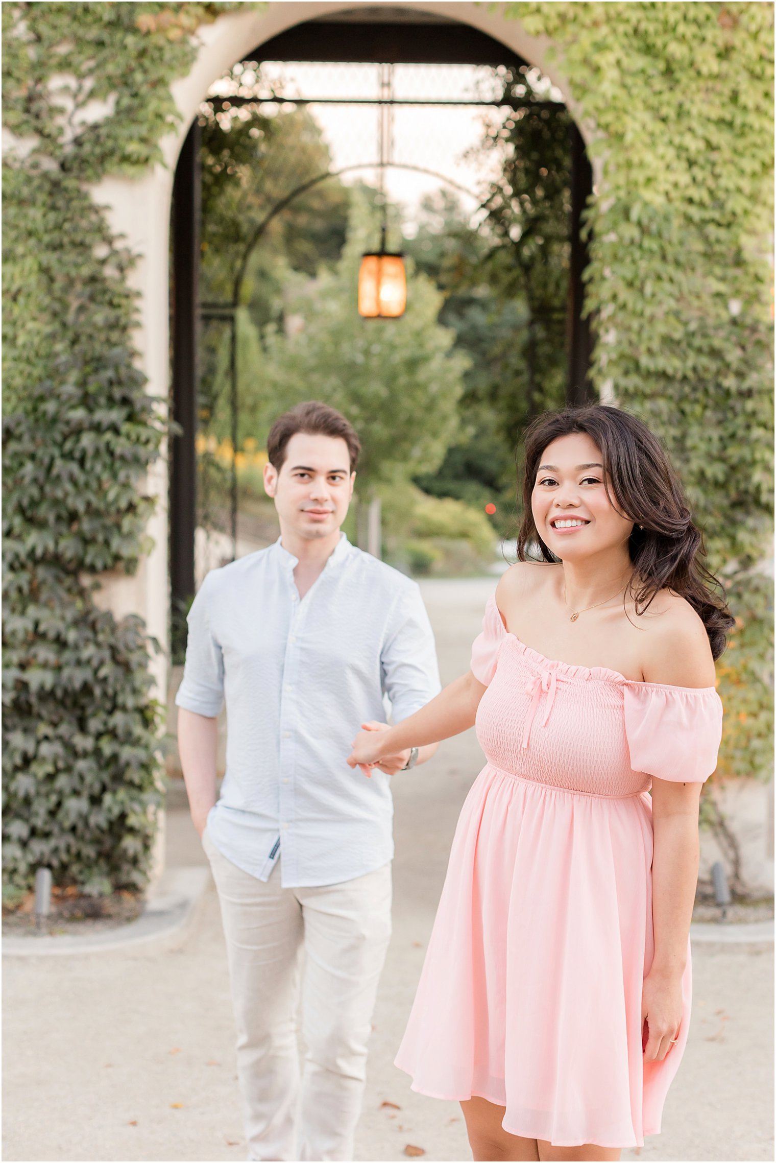 woman in pink dress walks with groom behind her near gate at Longwood Gardens