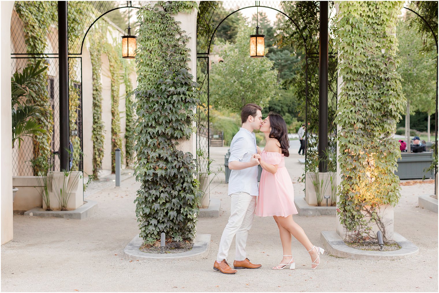 engaged couple kisses by wrought iron fence outside Longwood Gardens