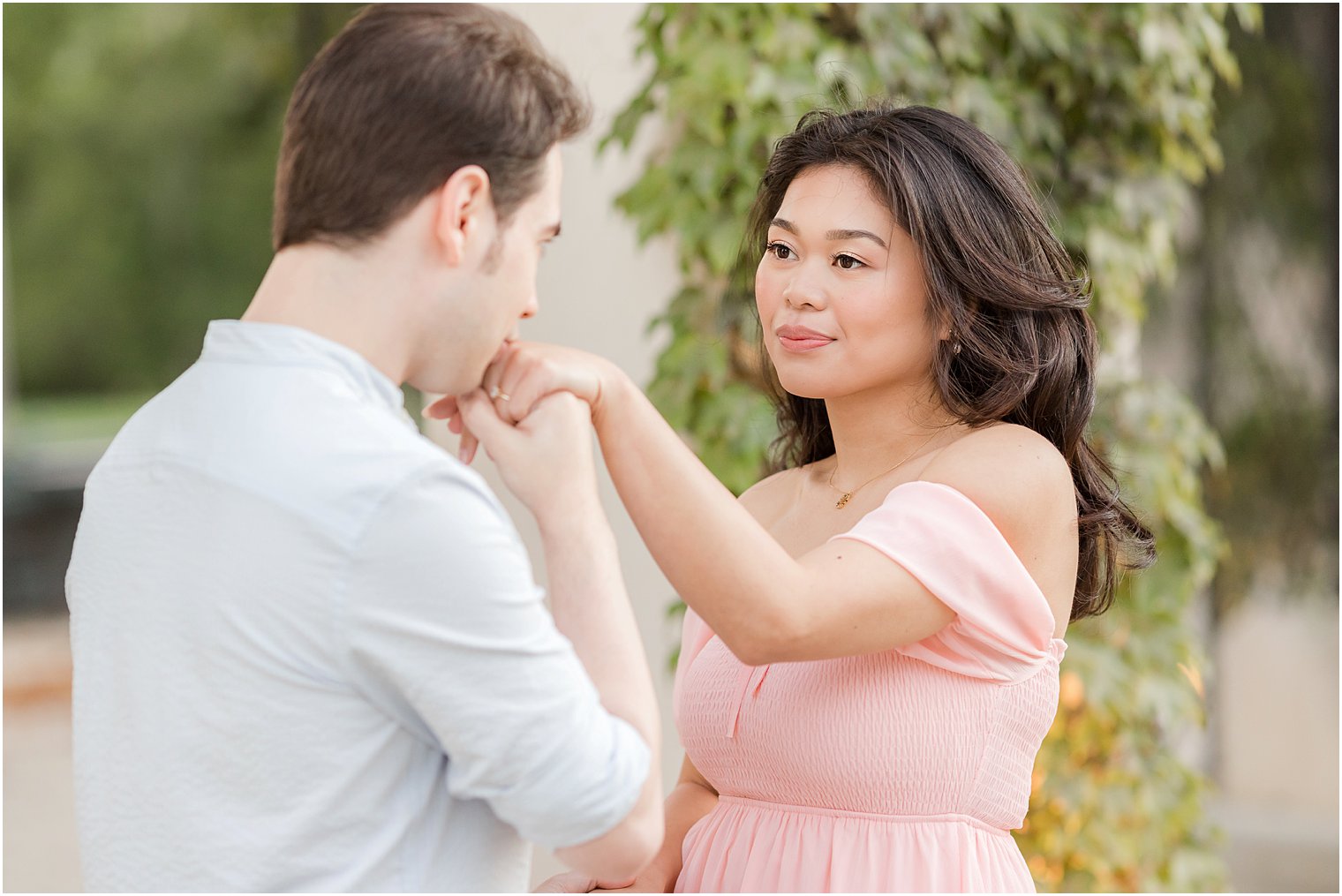man in blue shirt kisses woman's hand in pink dress 