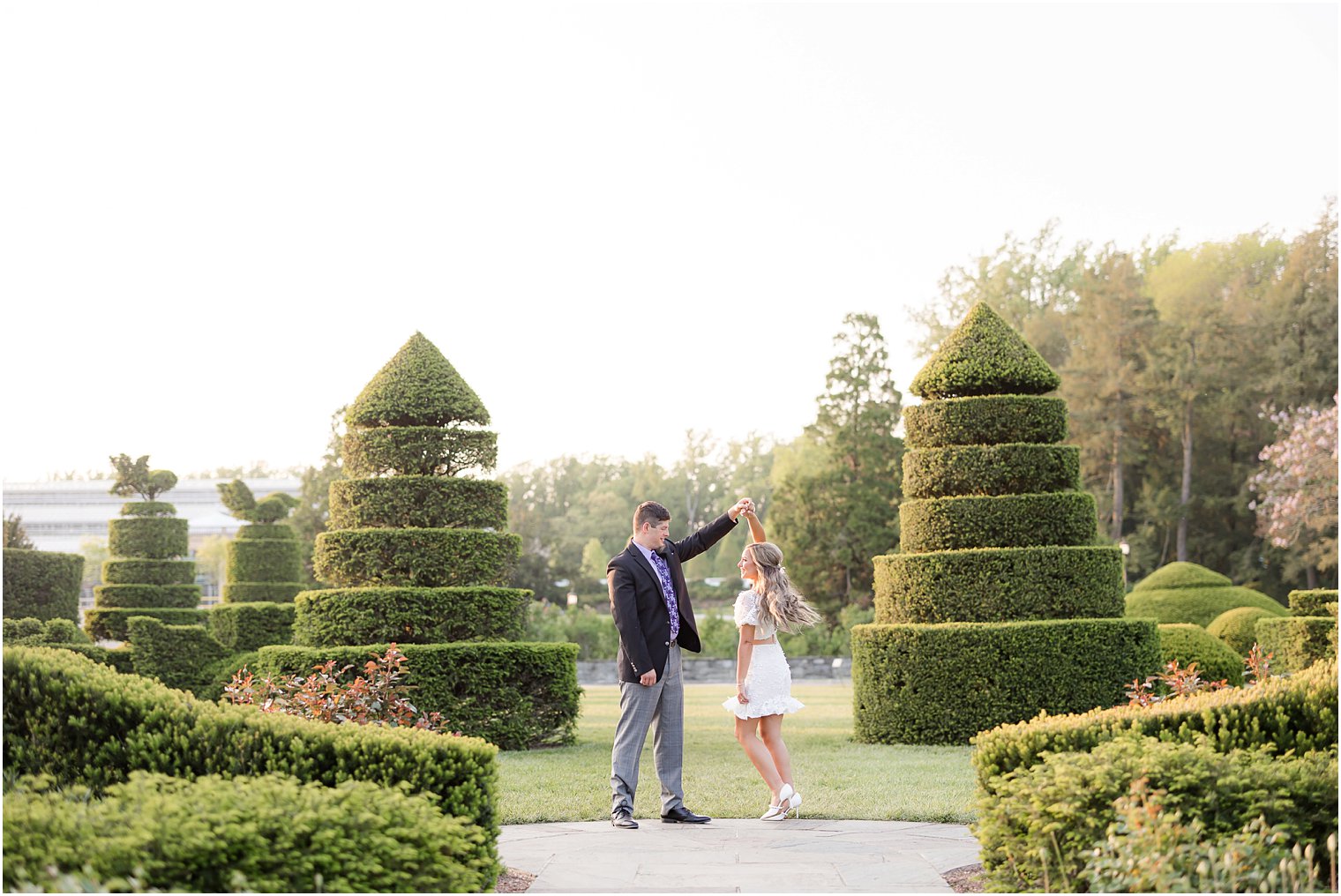 groom twirls bride in between topiaries at Longwood Gardens