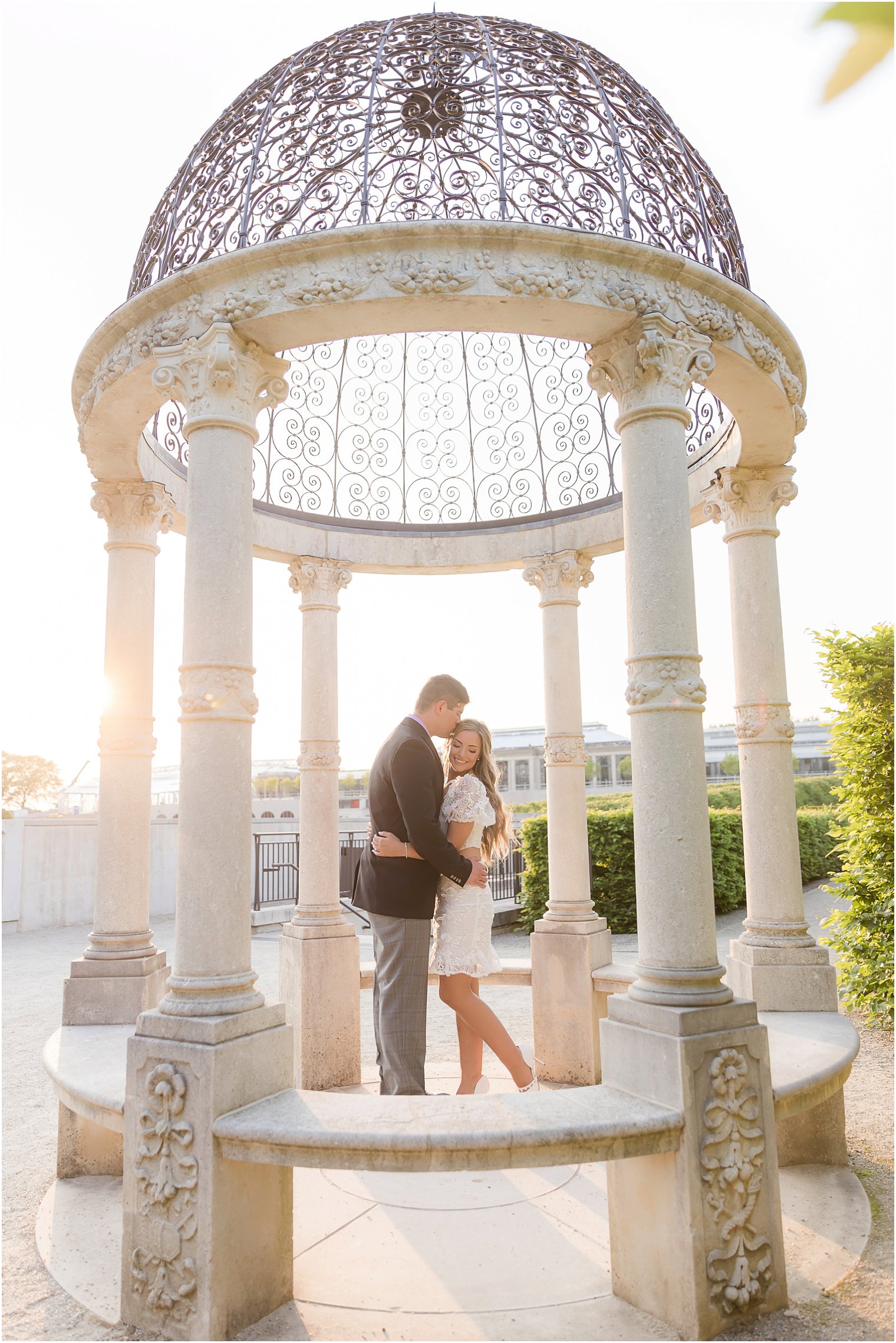 engaged couple hugs in gazebo with wrought iron top at Longwood Gardens