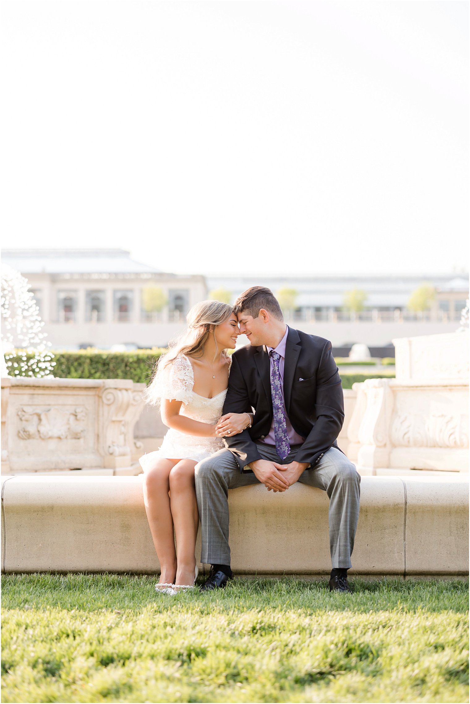 bride and groom sit together on fountain at Longwood Gardens