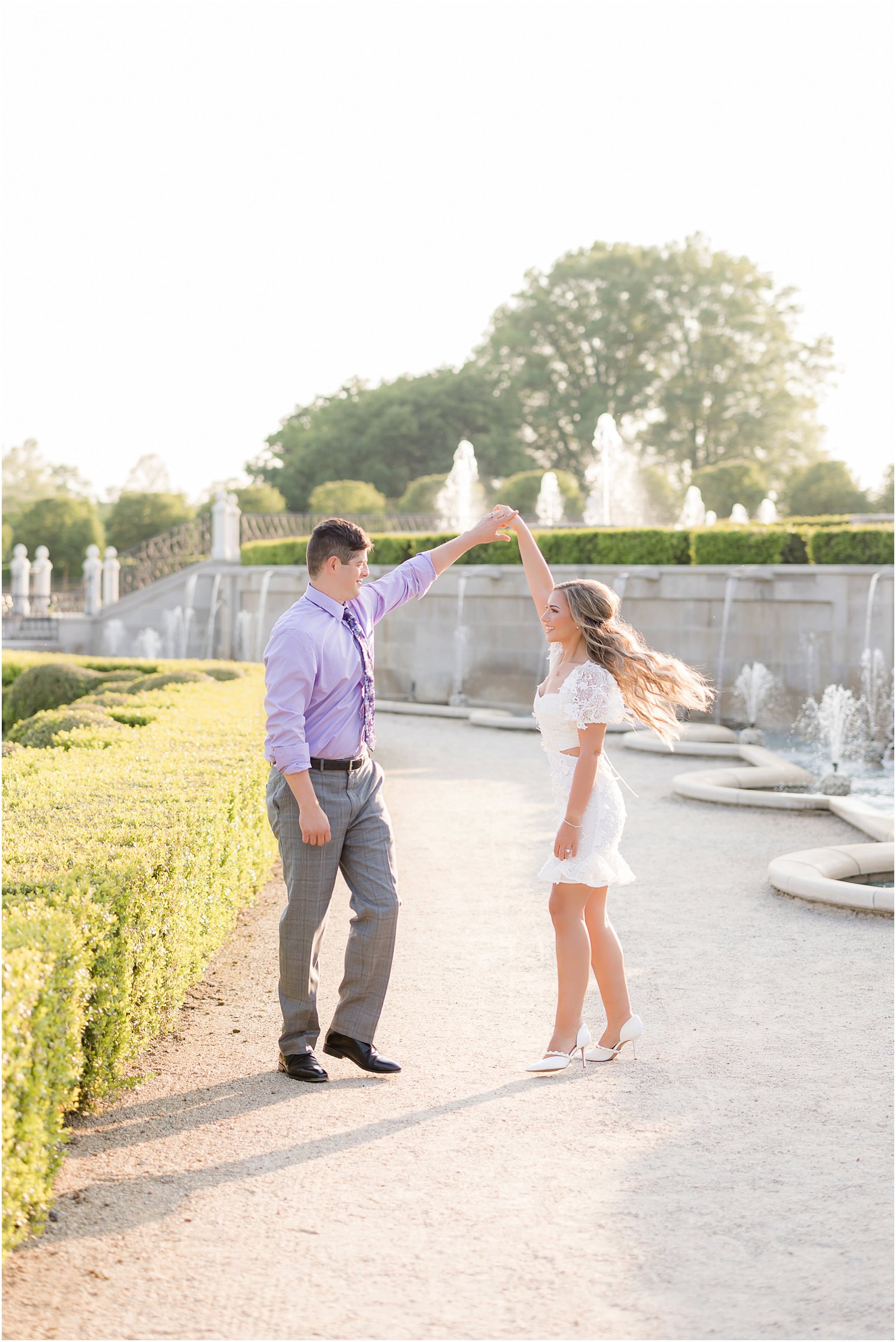 groom in purple button down shirt twirls bride in short white dress at Longwood Gardens